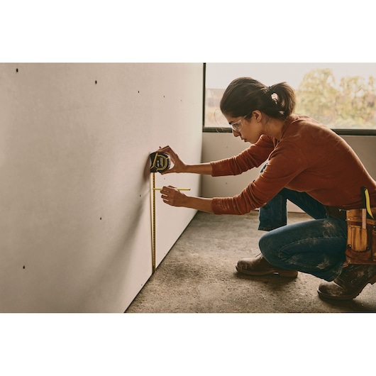 Photo of person using STANLEY 30-626 tape measure to mark measurements on drywall, construction setting.