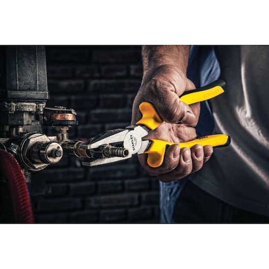 Photo of STANLEY 70-488 combination pliers with yellow handles being used to grip a metal fitting.