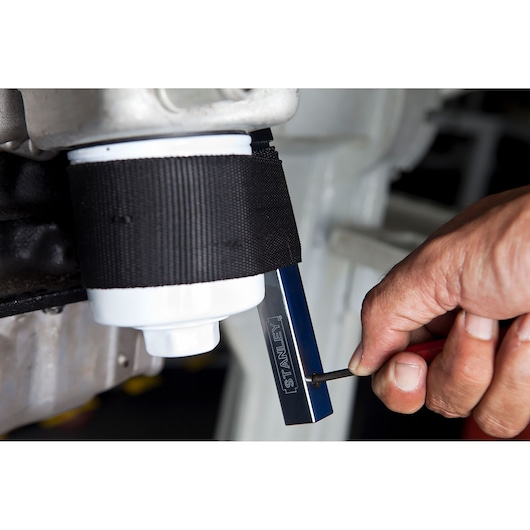 Photo of STANLEY oil filter wrench 78-230 in use on a white filter, close-up of hand adjusting the tool.