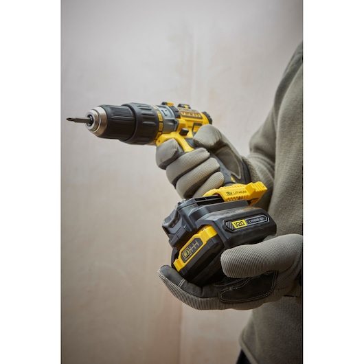 STANLEY SBA100 cordless drill held in gloved hands, yellow and black, side angle, photography product.