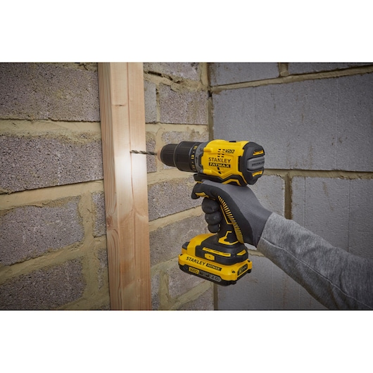 STANLEY SBD715C2K-B2 cordless drill being used to drill wood on brick wall, side view.