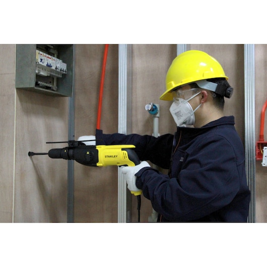 STANLEY SHR264 rotary hammer drill used by a worker in safety gear drilling into a wall during installation.