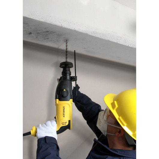 STANLEY SHR264 rotary hammer drill in use, yellow and black, held by worker drilling into concrete ceiling.