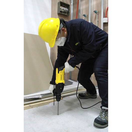 STANLEY SHR264 rotary hammer drill used by worker in safety gear drilling into concrete floor on jobsite.