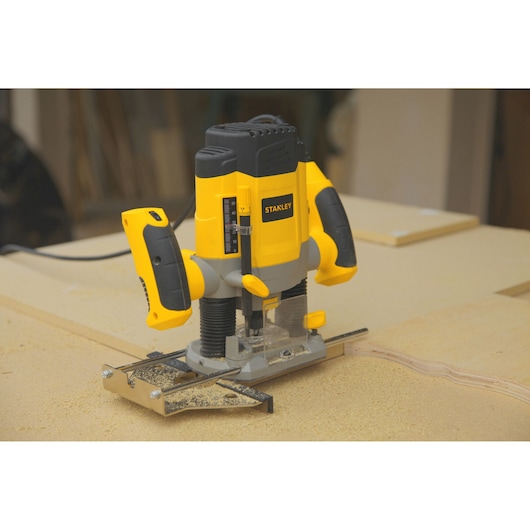 Photo of STANLEY SRR1200-AR plunge router with yellow and black body on wood surface in workshop.