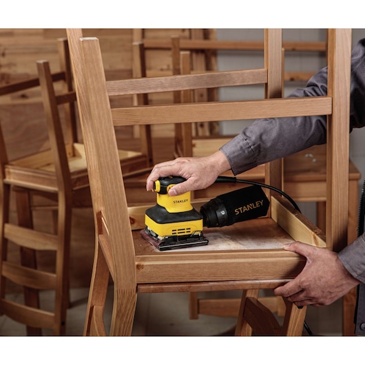 Photo of STANLEY SS24-B3 sander used on a wooden chair, handheld, woodworking context.
