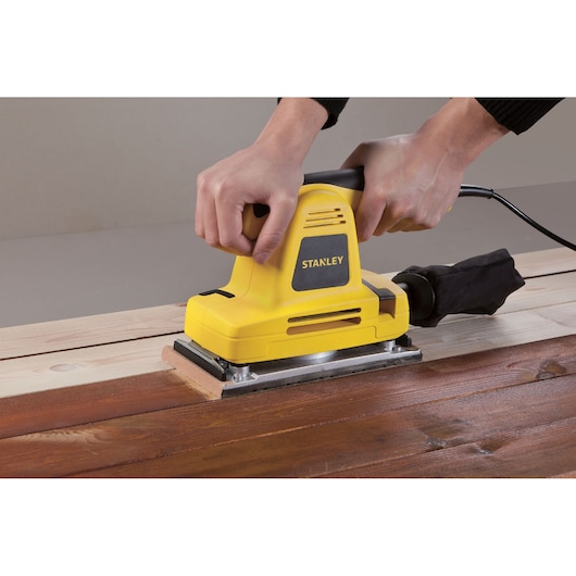 Photo of STANLEY SSS310 yellow sheet sander used on wooden surface, shown from side angle.