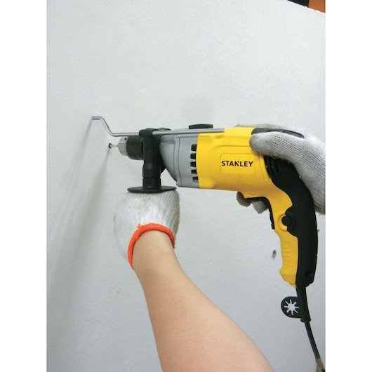 Stanley STDH8013 yellow and black corded drill in use on white wall, power tool category, side angle.