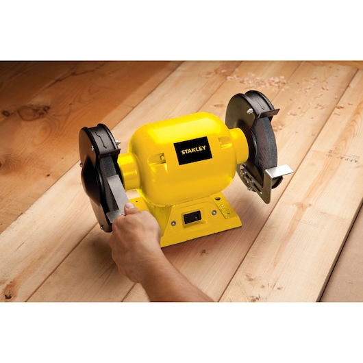 STANLEY STGB3715 yellow bench grinder in use on wood surface, close-up side view.