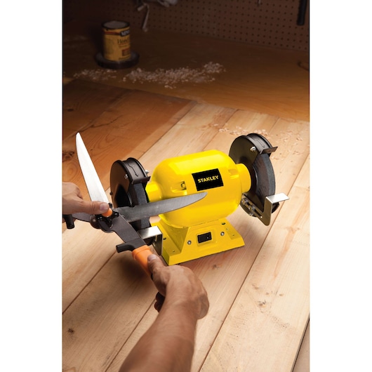 STANLEY STGB3715 bench grinder in yellow used to sharpen scissors on workbench, front angle view.