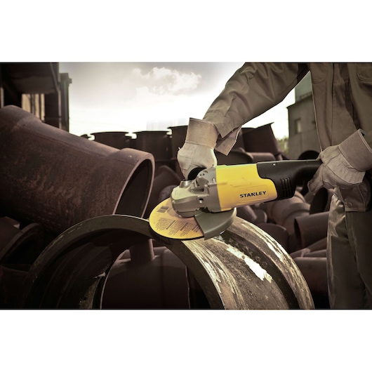 STANLEY STGL2223 angle grinder in use cutting large metal pipe outdoors, close-up view.