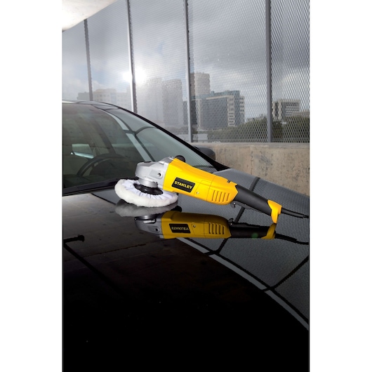 STANLEY STGP1318K yellow car polisher resting on a car hood outdoors.