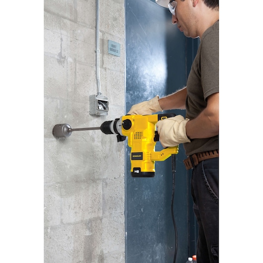 STANLEY STHR1232K rotary hammer drill in use drilling into concrete wall, side view.