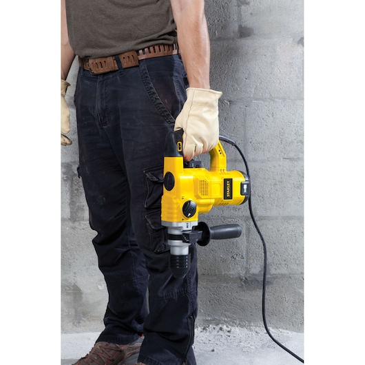 Photo of STANLEY STHR1232K rotary hammer drill held by person wearing gloves, shown in worksite setting.