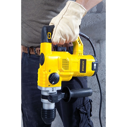 Photo of STANLEY STHR1232K rotary hammer drill in yellow and black, held by a gloved hand, front angle view.
