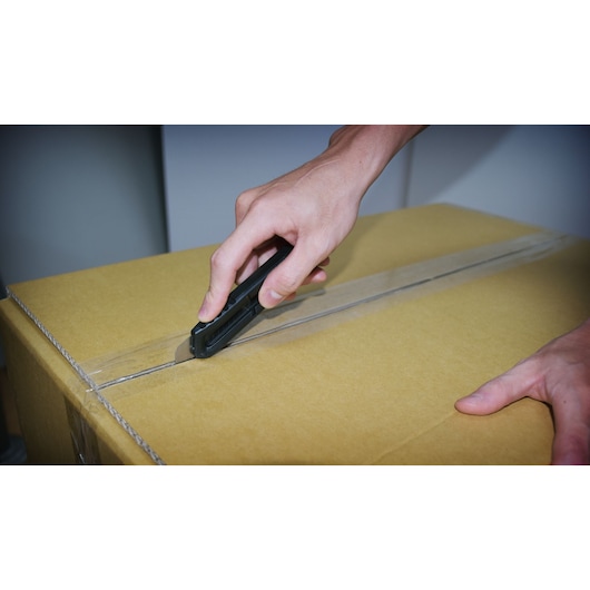 Photo of STANLEY STHT10323-840 utility knife cutting tape on a cardboard box, product in use, close-up view.