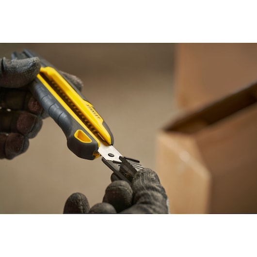 Photo of STANLEY STHT10501 snap-off utility knife with black and yellow handle held by gloved hands.
