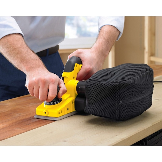 Photo of STANLEY STPP7502-B2 hand planer with black dust bag sanding wooden surface, close-up in use.