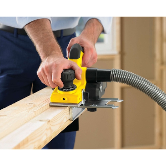 Photo of STANLEY STPP7502-B2 yellow hand planer smoothing wood, hose attached, woodworking setting.