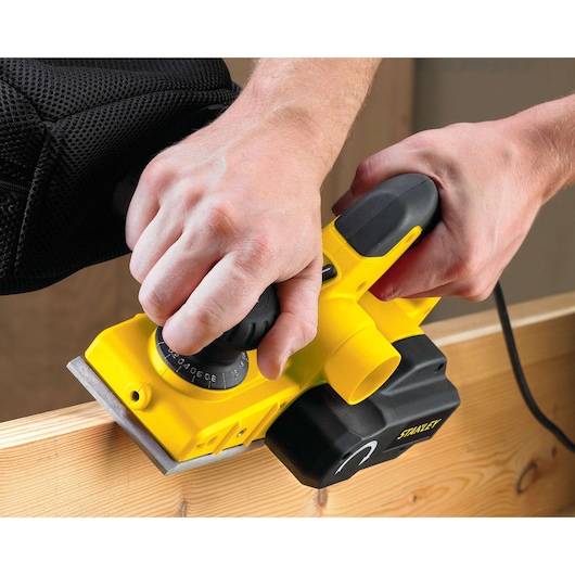 Photo of STANLEY STPP7502-B2 electric planer in use on a wood surface, showing ergonomic grip and adjustment knob.