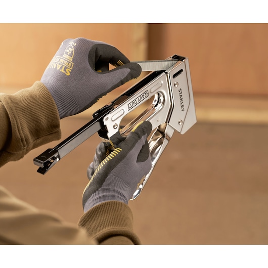 Stanley TR110 heavy duty stapler held in gloved hands, side angle, loading staples.